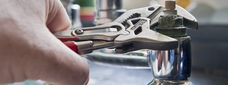 Close up of a hand gripping a tap using a spanner